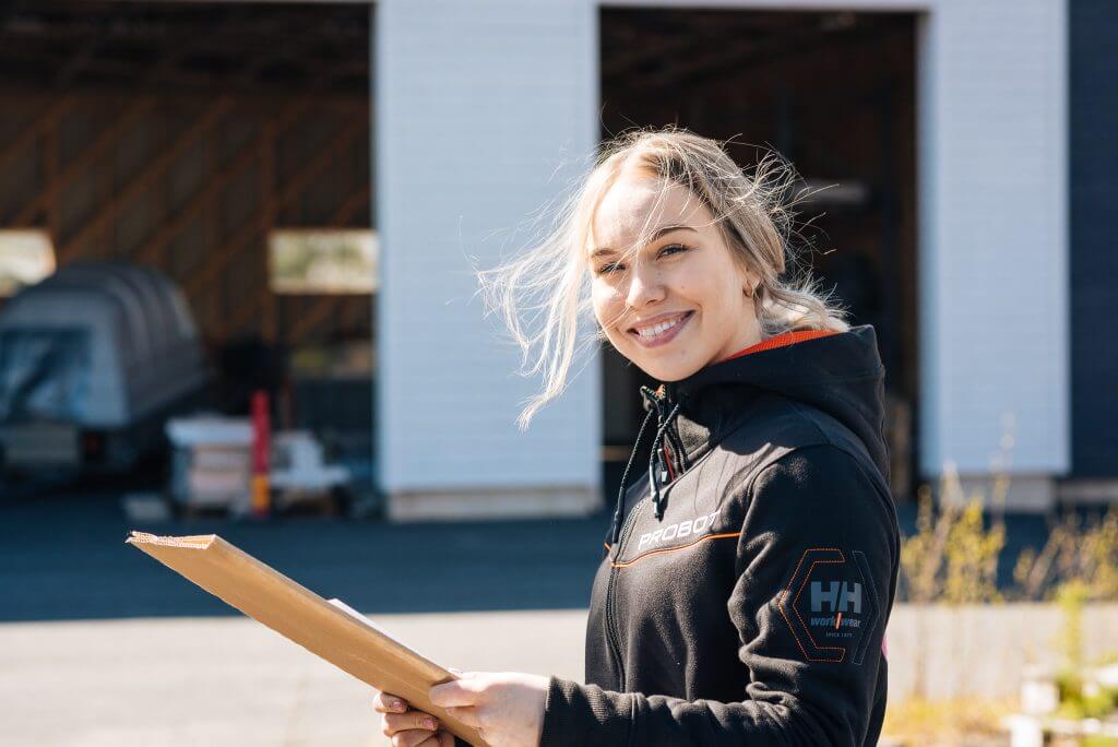 A woman smiles at the camera outdoors, holding a writing pad in her hands.