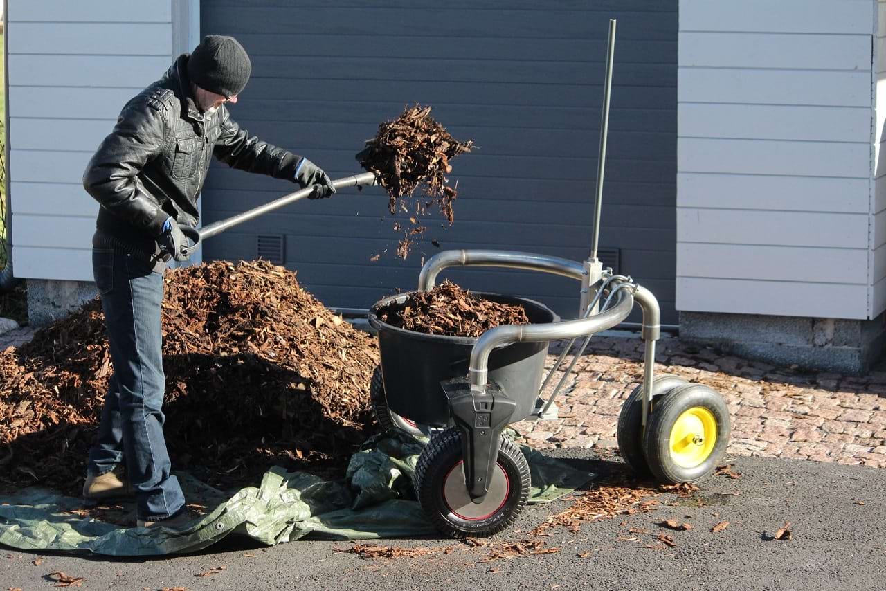 A man uses a shovel to lift wood chips onto a mobile robot.