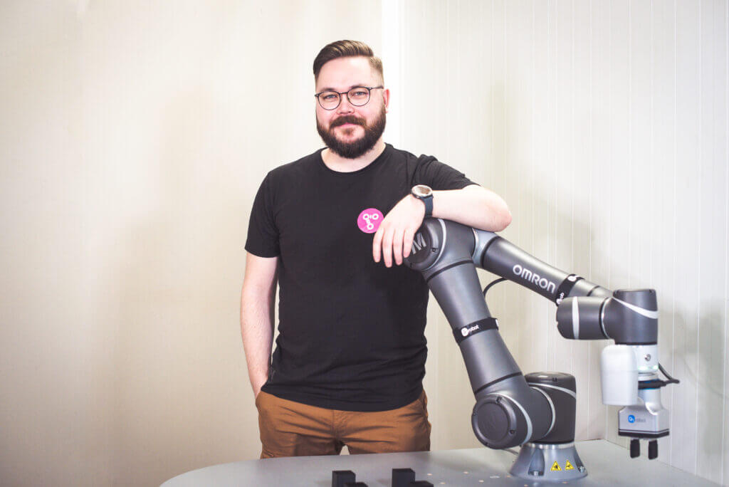 A man standing behind a table and leaning to an OMRON cobot, pondering "Will robots steal your job?"