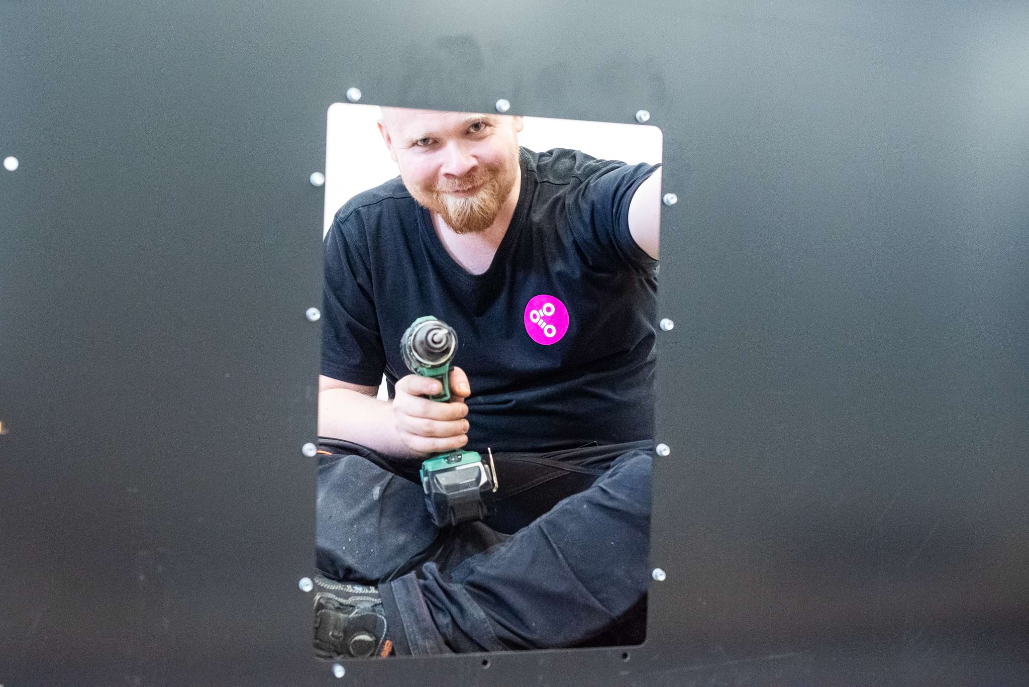 In the foreground, a metal plate with a man holding a drill peering through the gap.