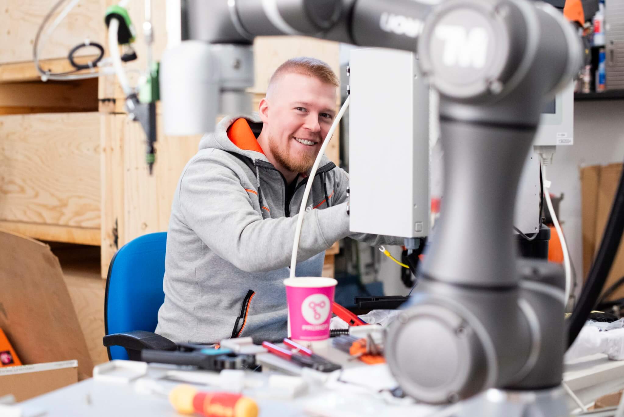 Ville työntouhussa Probot Oy:n hallilla. Etualalla on Omron:in yhteistyörobotti.