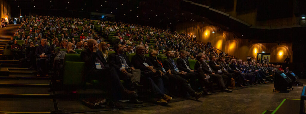 A lot of people are sitting in a dimly lit auditorium at European Robotics Forum 2023