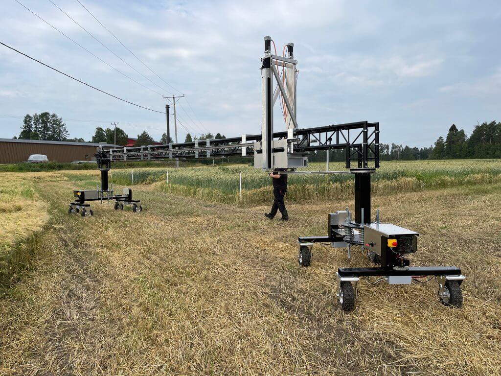 Iso peltorobotti kulkee pellolla. Ihminen kävelee robotin takana ohjaten sitä ohjaimella.