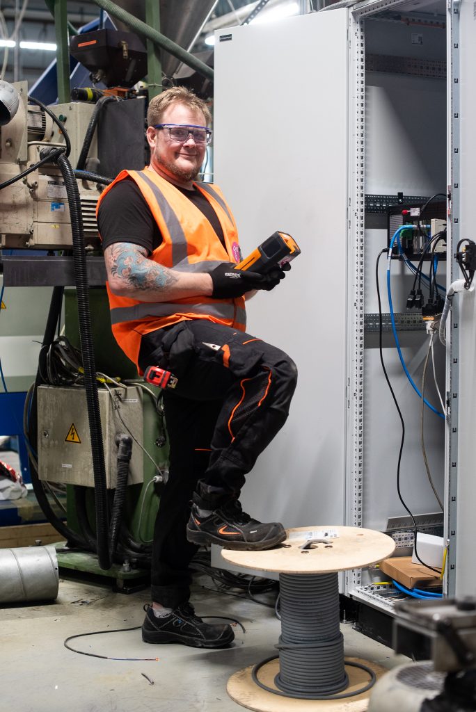 Happy employee poses at a factory, wearing safety glasses and safety vest.