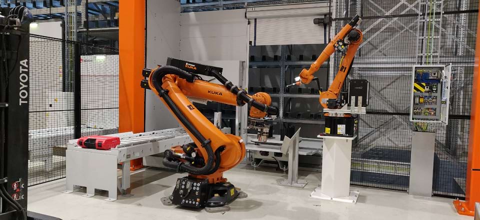 The picture shows two industrial robots in a fenced area.