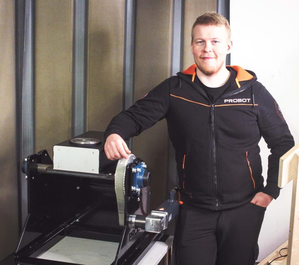 An employee smiles next to a machine.