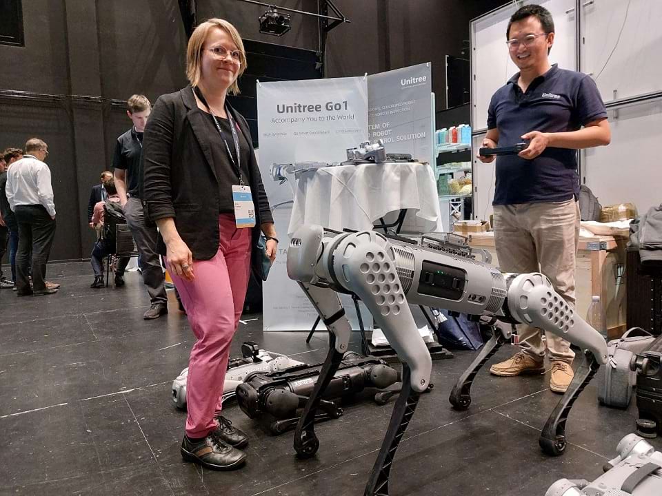 Pinkki housuinen nainen tapaa ERF2023 -messuosastolla unitreen b1 -mallin robottikoiran