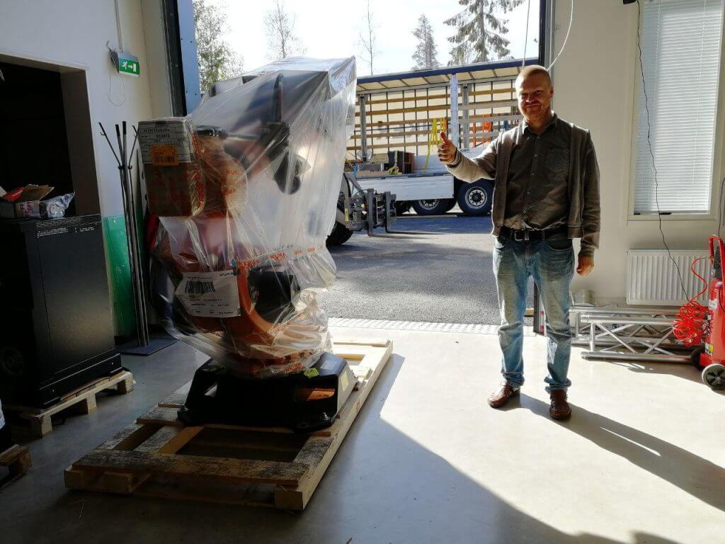 Happy man stands next to wrapped industrial robot and holds his thumb up.