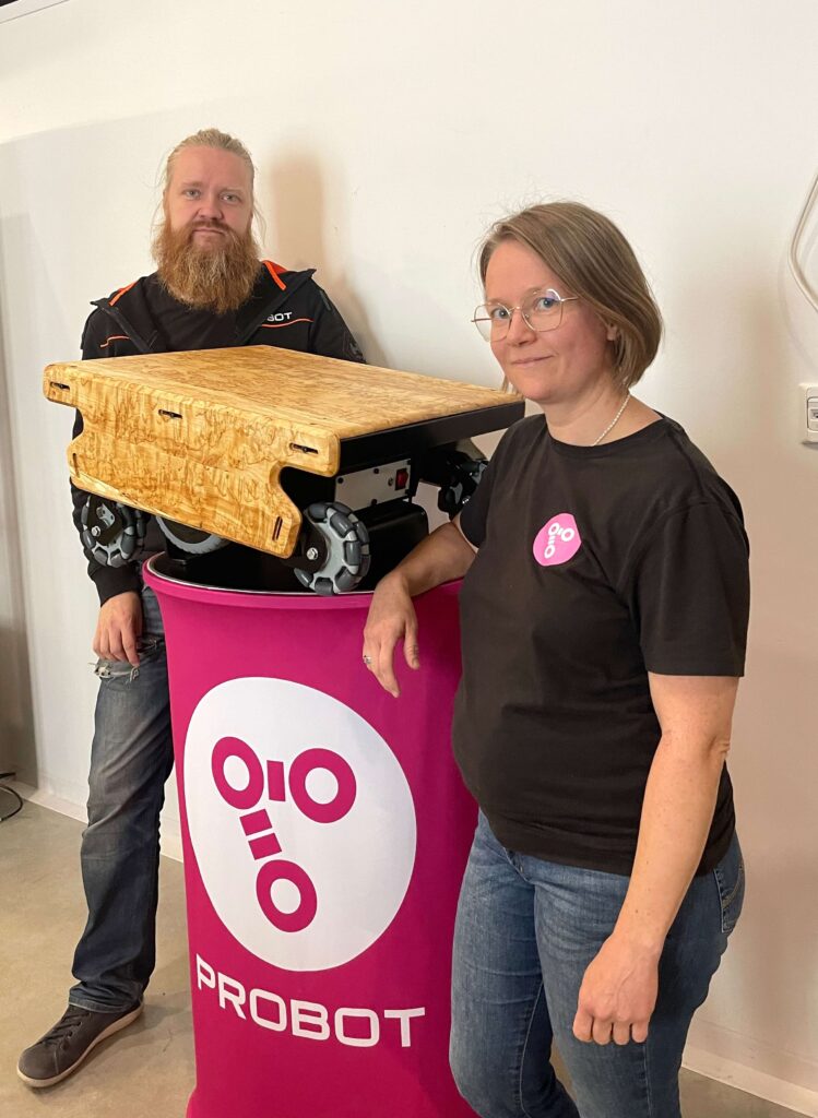 Two people showcasing an innovative mobile robot with a wooden casing. The mobile robot is placed on a table featuring the Probot logo.