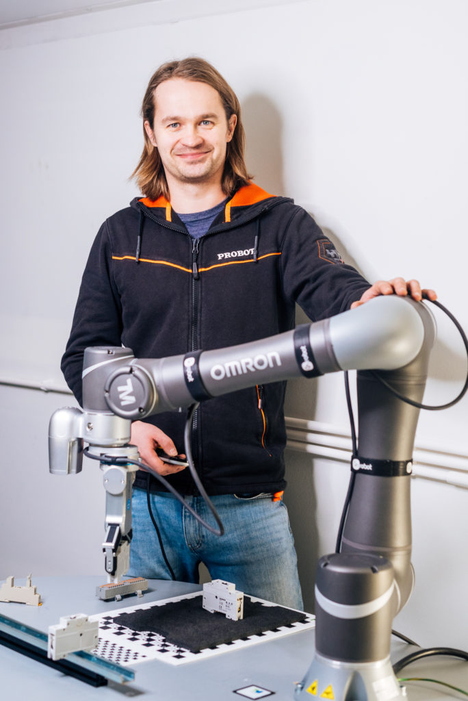 An employee smiles at the camera and holds his hand over the Omron cobot.