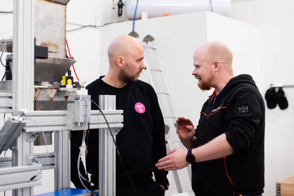 Two robotics professionals discussing in front of industrial equipment in a production environment.
