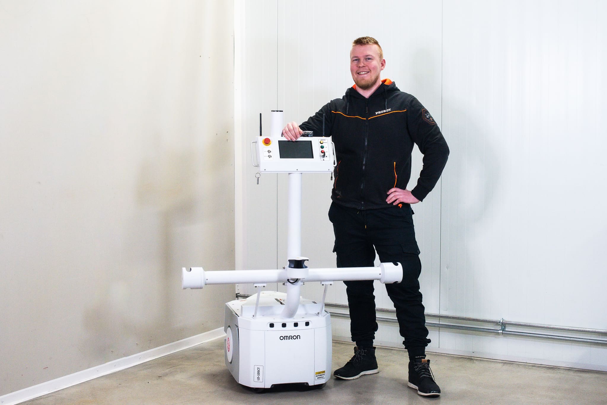 A man smiles and leans on a white mobile robot.