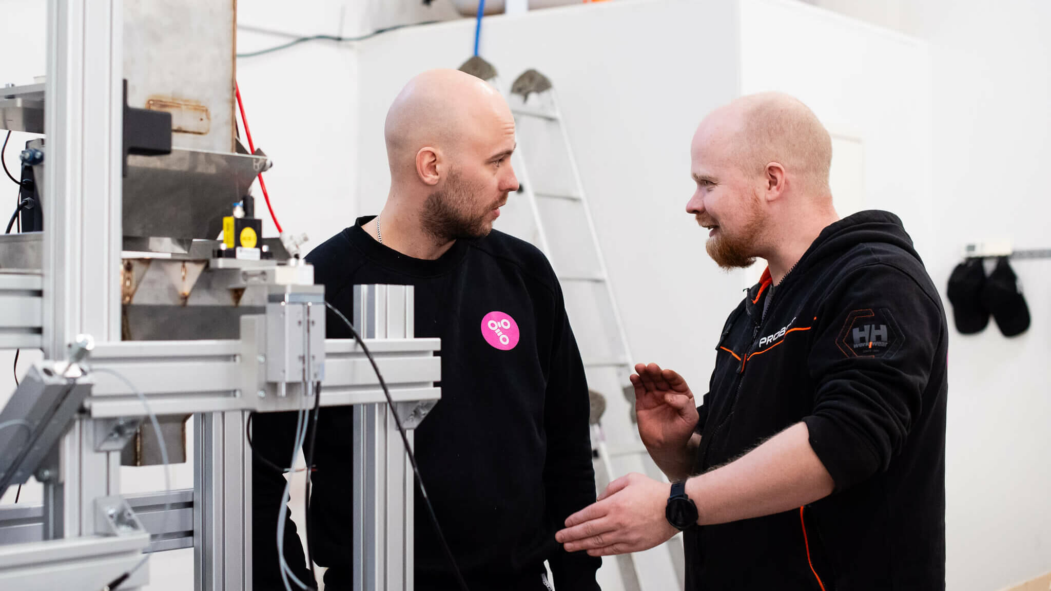 Kaksi robotiikka-alan asiantuntijaa keskustelevat tuotantolaitteiston äärellä teollisuusympäristössä.
