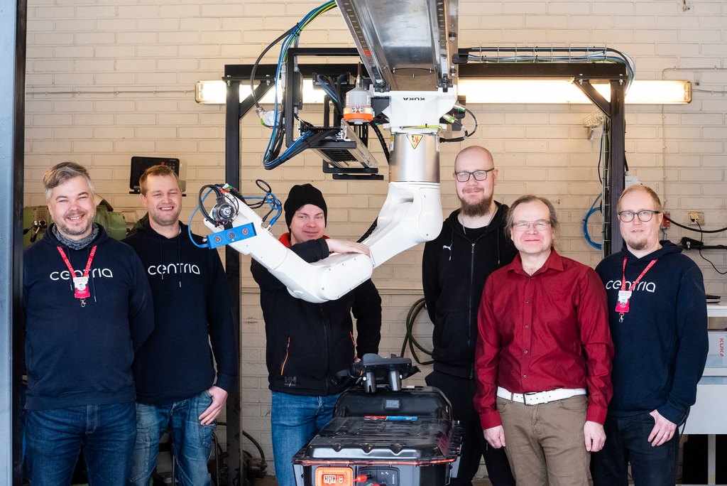 Six experts pose in a row behind the robot.