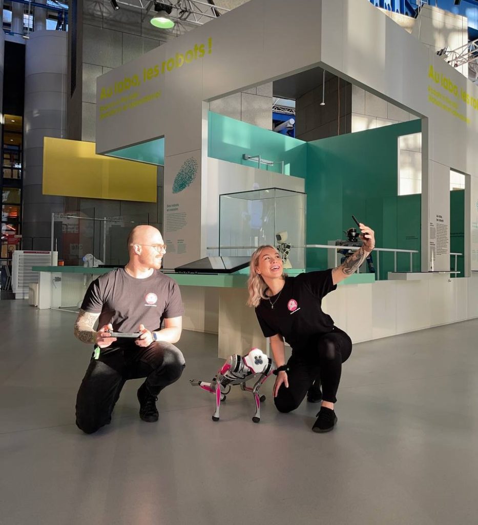 Woman is taking a selfie with a robot dog and her colleague.