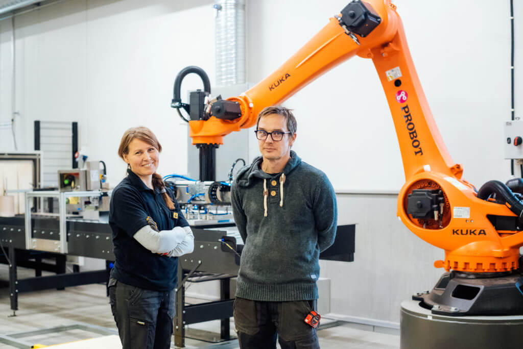 A woman and a man stand in front of a robot cell