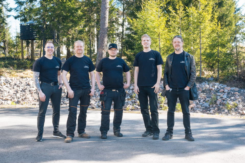 Five happy team members pose outdoors.