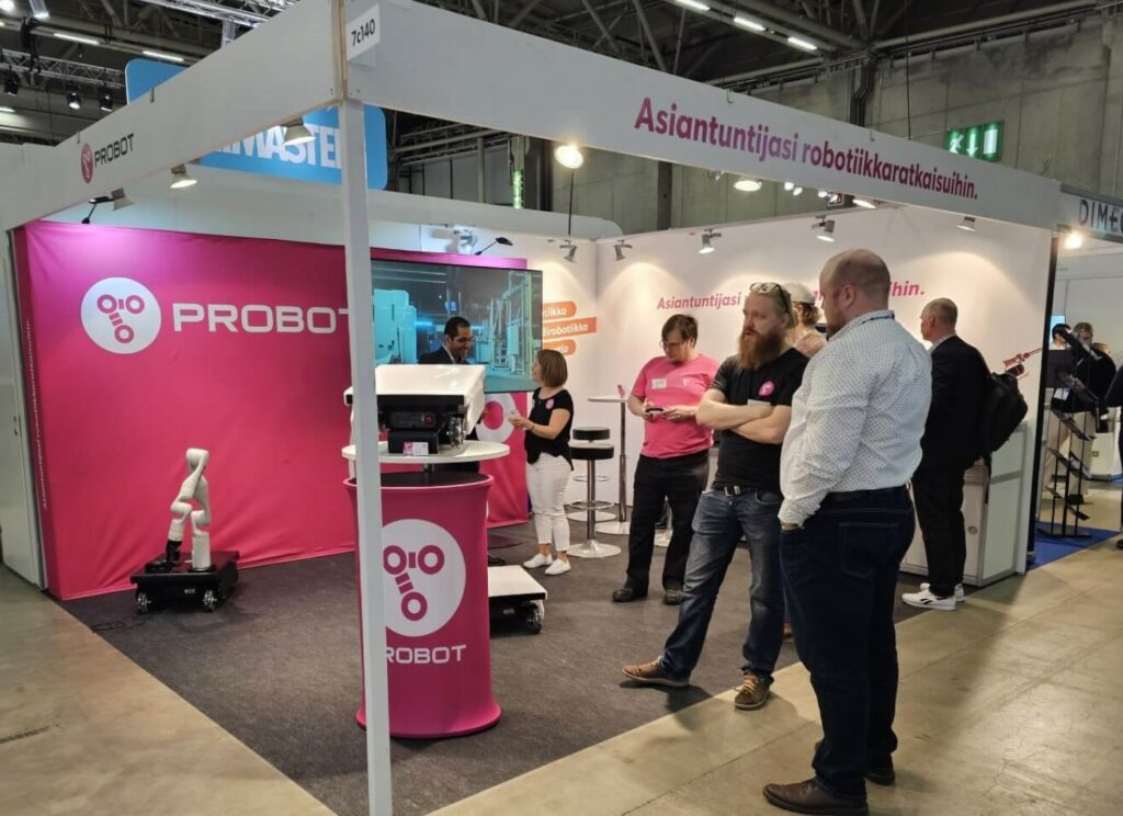 A fair stand, people and a black mobile robot Dolly with a white robotic arm.
