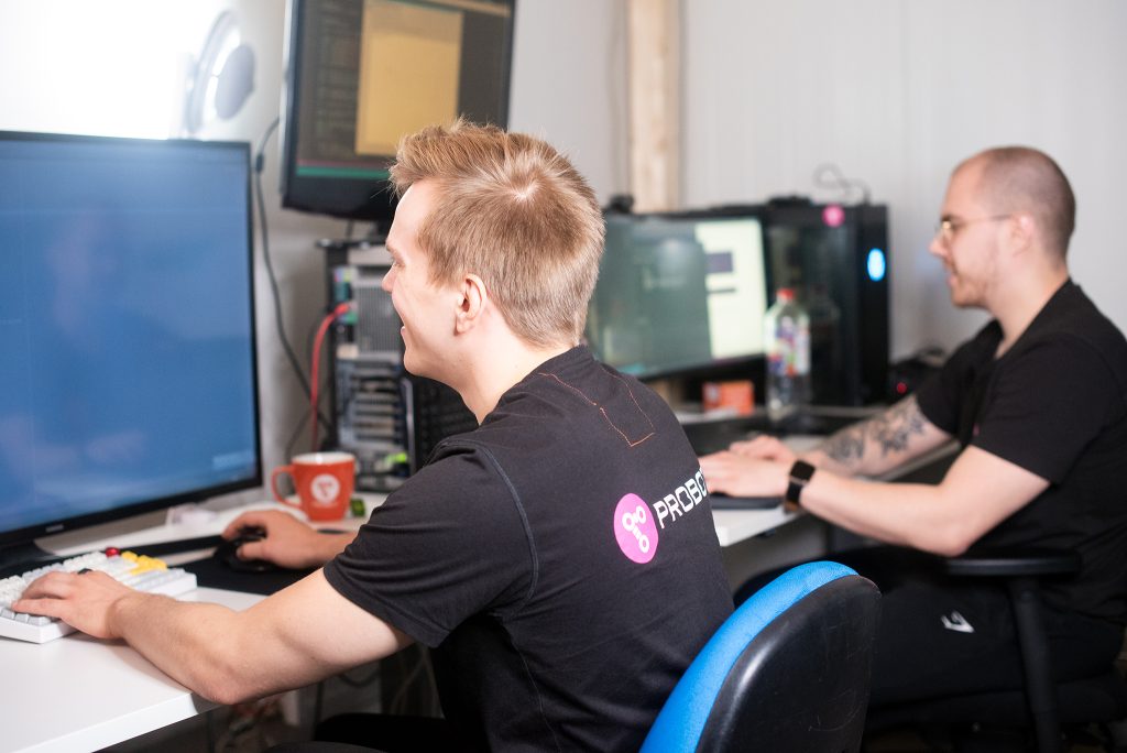 Two smiling men work side by side at their workstations.